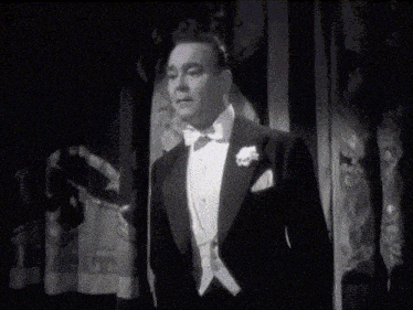 a man in a tuxedo stands in front of a window