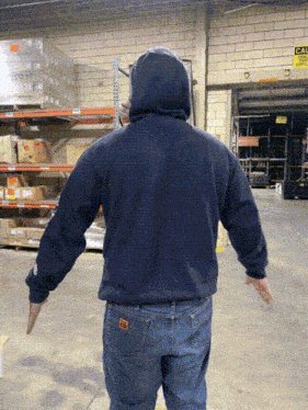 a man in a blue hoodie is standing in a warehouse with his arms outstretched in front of a sign that says exit