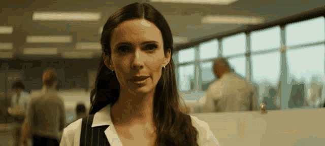a woman in a white shirt is standing in a room with a lot of windows