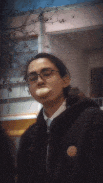 a person wearing glasses and a black jacket has a piece of food in his mouth