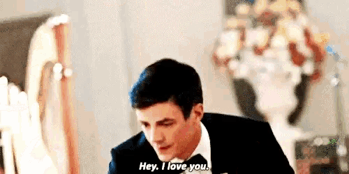 a man in a suit and bow tie is saying `` hey , i love you '' while sitting at a table .