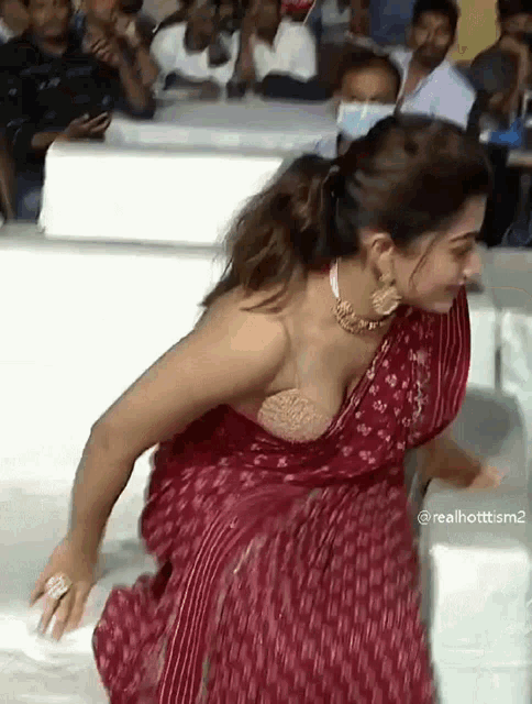 a woman in a red saree is sitting on a white couch in front of a crowd .