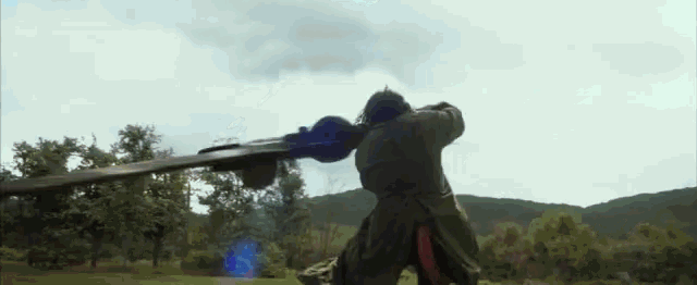 a man is holding a sword in a field with trees in the background .