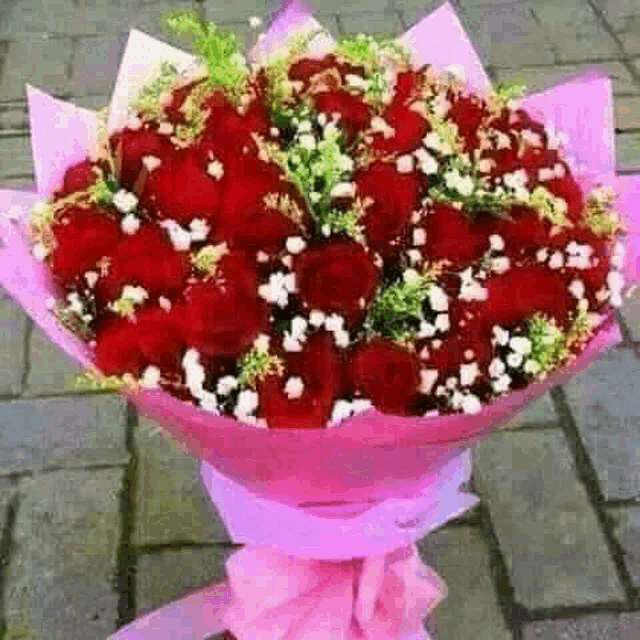 a bouquet of red roses wrapped in pink paper on a sidewalk .