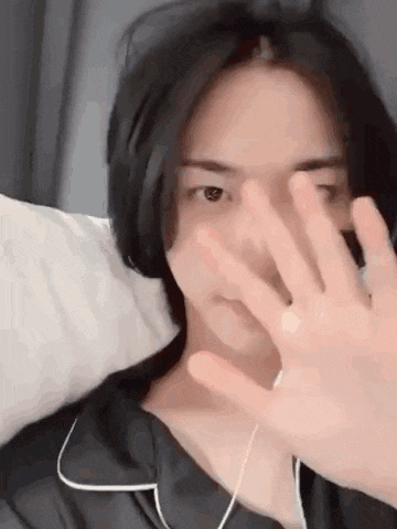 a young man is covering his face with his hand while laying in bed .