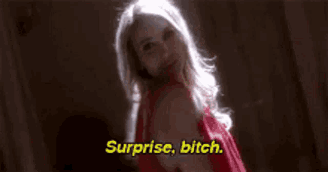 a woman in a red dress is standing in a dark room and saying surprise , bitch .