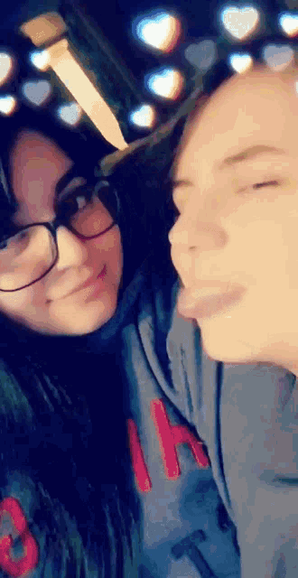 a man and a woman are posing for a picture with their tongues out . the woman is wearing glasses .
