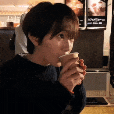 a person drinking from a cup with a sign in the background that says ' cafe menu '