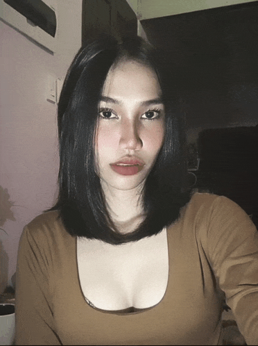 a woman with black hair is wearing a brown top with a plunging neckline