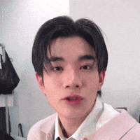 a young man is making a funny face while wearing a pink jacket and white shirt .