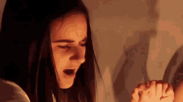 a woman is praying in a dark room with her hands folded .