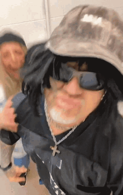 a man wearing a hat and sunglasses has a cross on his neck