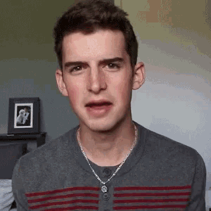 a young man wearing a striped shirt and a chain around his neck looks at the camera
