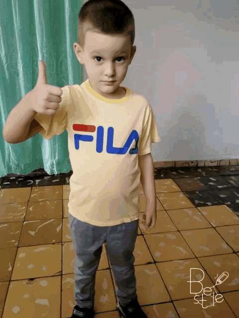 a young boy wearing a yellow fila t-shirt gives a thumbs up