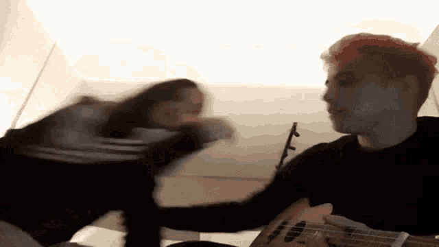 a man with red hair is playing an ukulele while a woman holds his hand .