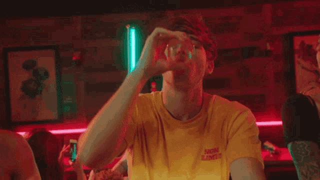 a man wearing a yellow t-shirt that says " atomic lovers " is sitting at a table with two women