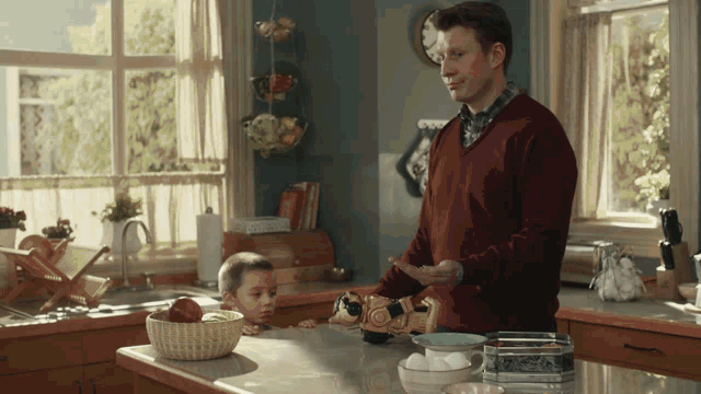 a man in a red sweater is standing in a kitchen next to a child