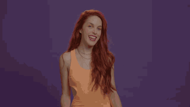 a woman in an orange tank top is making a heart shape with her fingers