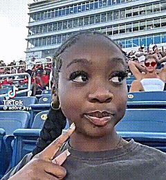 a young girl is sitting in a stadium with a crowd watching a baseball game .