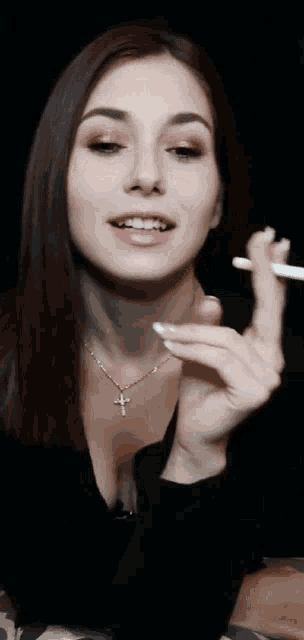 a woman is smoking a cigarette with a cross necklace on her neck .