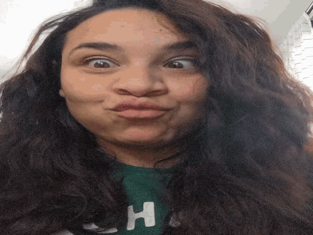 a woman wearing a green shirt with the letter h on it making a funny face