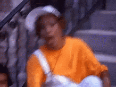 a woman in an orange shirt and white hat is sitting on the stairs .