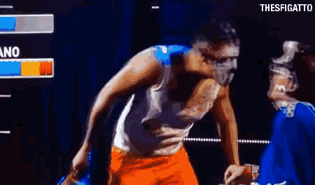 a man in a white tank top and orange shorts is fighting another man in a boxing ring with the hashtag thesfigatto