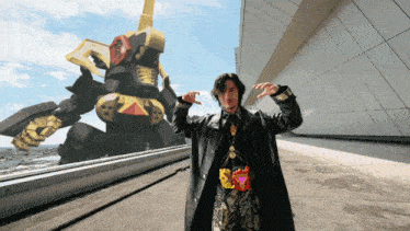 a man in a black coat stands in front of a giant robot