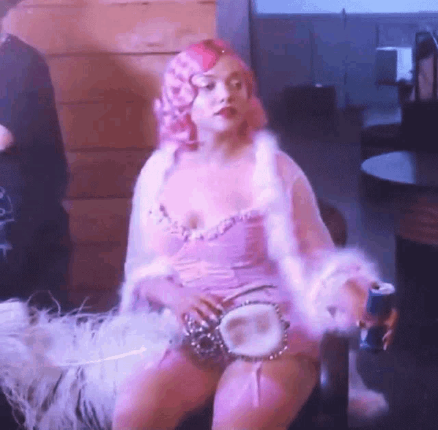 a woman with pink hair is sitting in a chair holding a can of coke