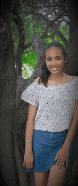 a girl in a white off the shoulder top and denim skirt smiles for the camera