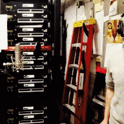 a man stands in front of a microphone in a room with a ladder in the background