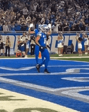 a football player in a blue uniform is running on the field with a crowd watching