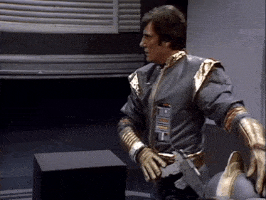 a man in a gray and gold costume is standing next to a black box