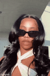 a woman wearing sunglasses and a white top is taking a picture of herself .
