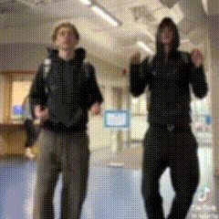 two men are dancing in a hallway and one has a hoodie on