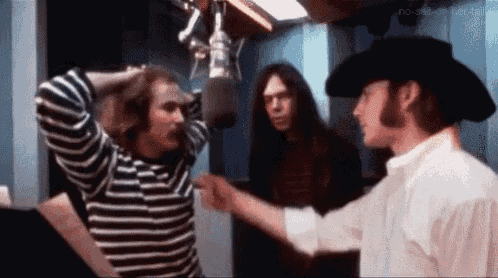 a group of men are standing next to each other in front of a microphone in a recording studio .