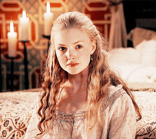 a woman with blonde hair is sitting on a bed with candles in the background