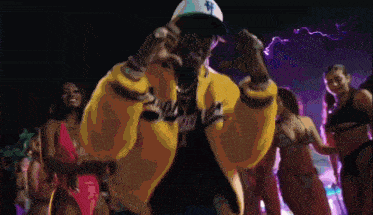 a man in a yellow jacket is standing in front of a group of women in bikinis ..