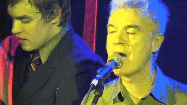 a man singing into a microphone while another man plays a guitar