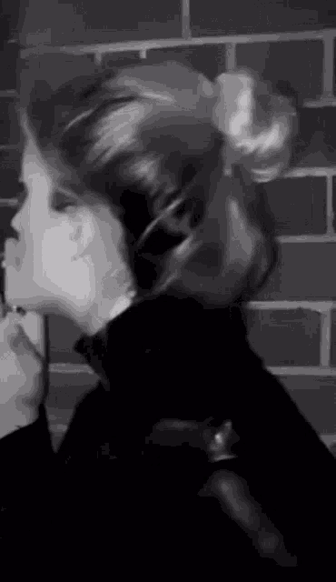 a woman with her hair in a bun is smoking a cigarette in front of a brick wall