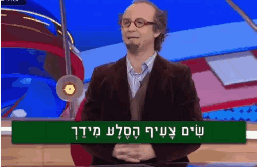 a man in a suit and glasses stands in front of a green sign that says ' shalom ' on it