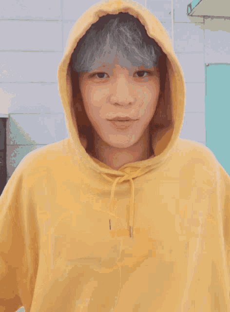 a young man wearing a yellow hoodie is giving a thumbs up sign