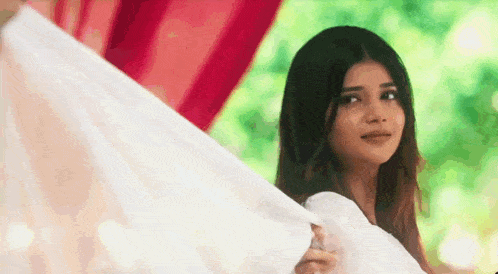 a woman in a white dress is holding a white cloth and looking at the camera .