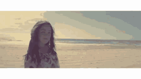 a young girl is standing on a sandy beach looking at the ocean .