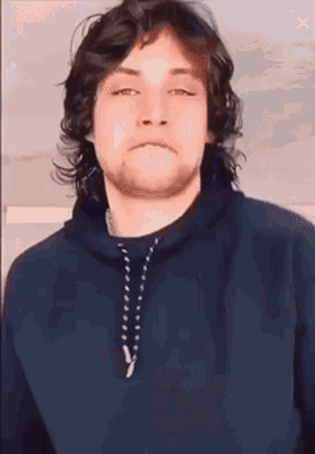 a young man with long hair and a beard is wearing a blue hoodie and a necklace .
