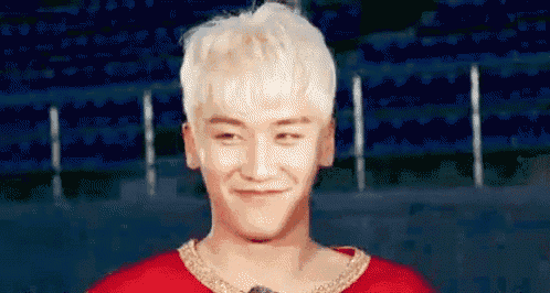 a man with blonde hair is wearing a red shirt and a gold necklace .