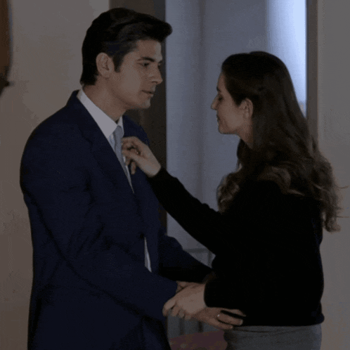 a man in a suit and tie is being helped by a woman in a black sweater