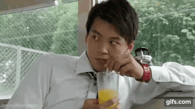 a man is drinking orange juice through a straw while sitting in a car .