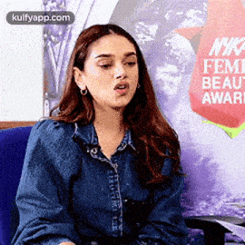 a woman in a denim shirt is sitting in a blue chair and making a funny face .