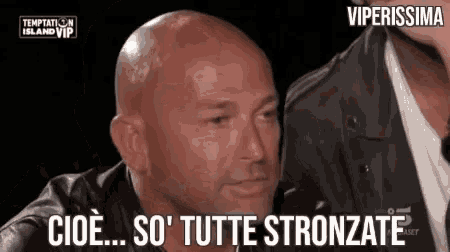 a bald man in a leather jacket is talking to another man in a foreign language .